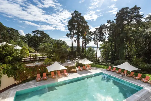 Außenpool umgeben von Sonnenschirmen und Liegestühlen mit Blick auf einen dichten Wald im Precise Resort Bad Saarow.