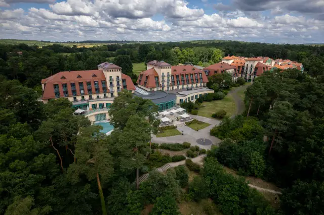 Aerial view of the Precise Resort Bad Saarow, nestled among forests, with a focus on the main building and the outdoor pool area.