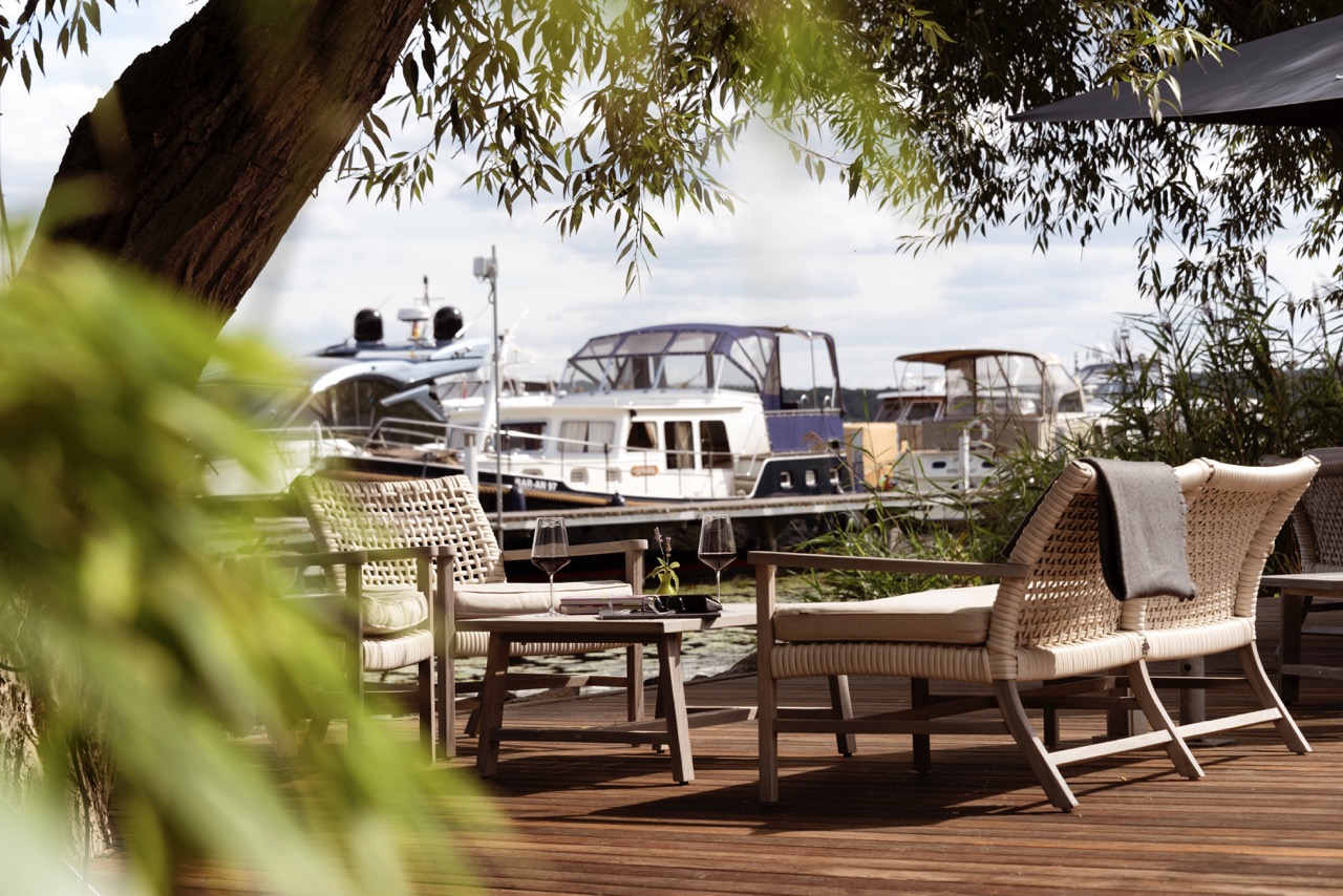 A cozy outdoor terrace of a lakeside beauty salon with plush seating and a picturesque view of moored yachts.