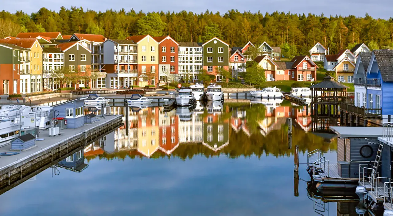 Malerische Hafensiedlung des Precise Resort Marina Wolfsbruch mit farbenfrohen Ferienhäusern entlang des Wassers.