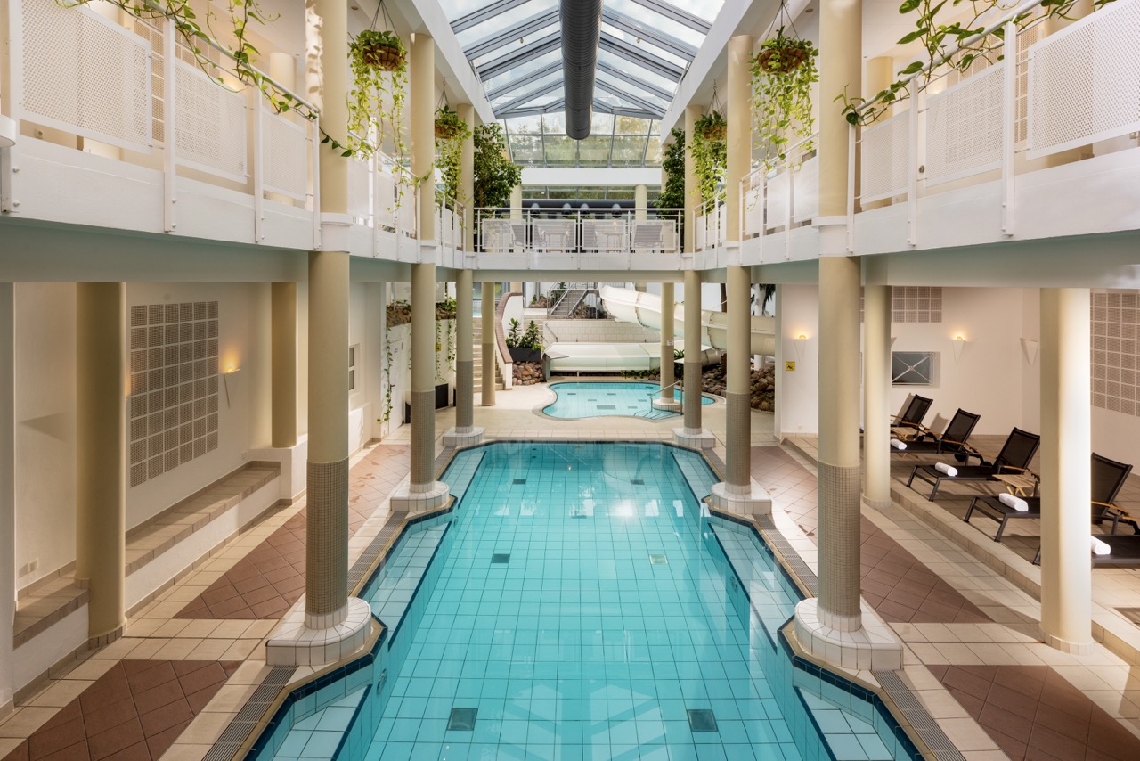 The indoor pool at Precise Resort Marina Wolfsbruch framed by an elegant gallery and tropical plants.