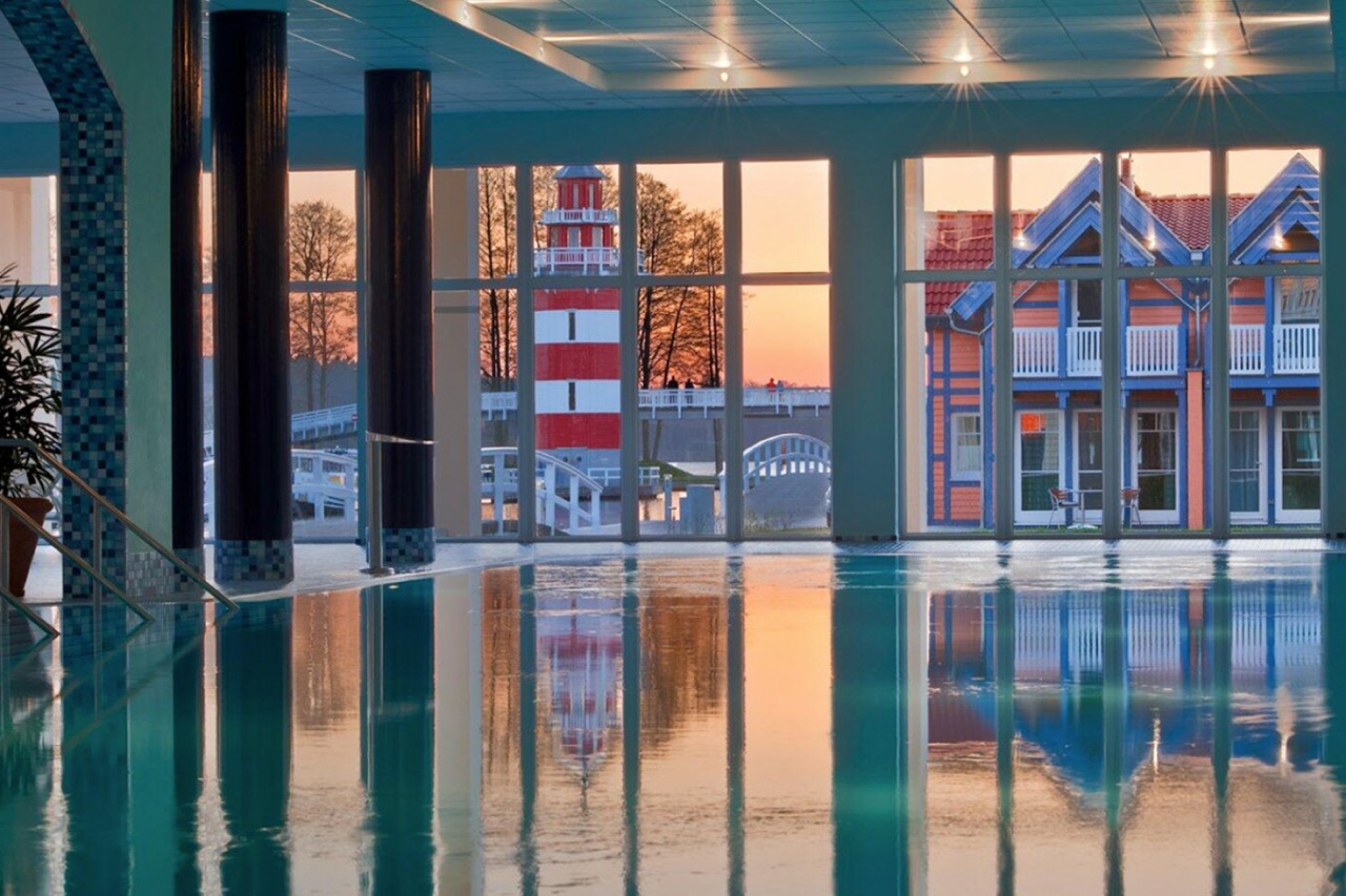 Der Innenpool des Precise Resort Hafendorf Rheinsberg schimmert im sanften Abendlicht mit Blick auf die farbenfrohen Häuser.