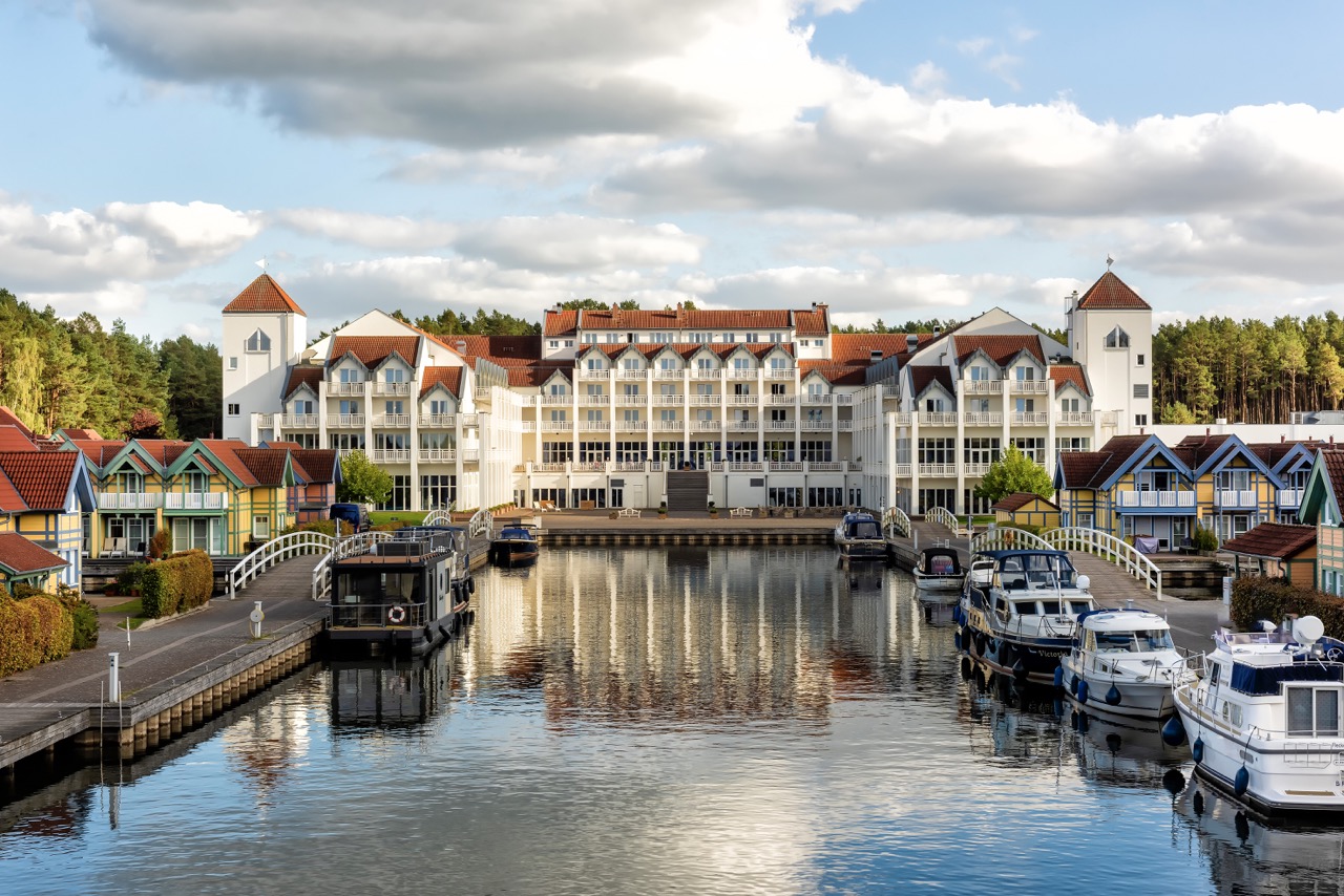 View of Precise Resort Hafendorf Rheinsberg with marina and traditional boats in the foreground.