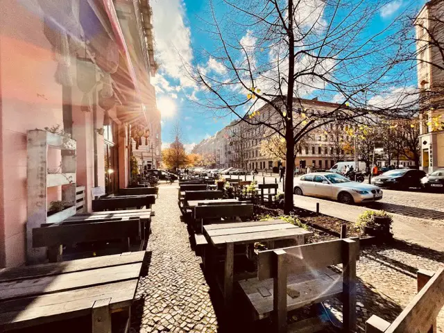 Sonnenbeschienene Terrasse eines Cafés in Berlin mit Blick auf eine belebte Straße.