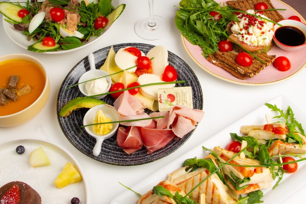 An assortment of diverse dishes including salads, soups, and sandwiches on a white table.