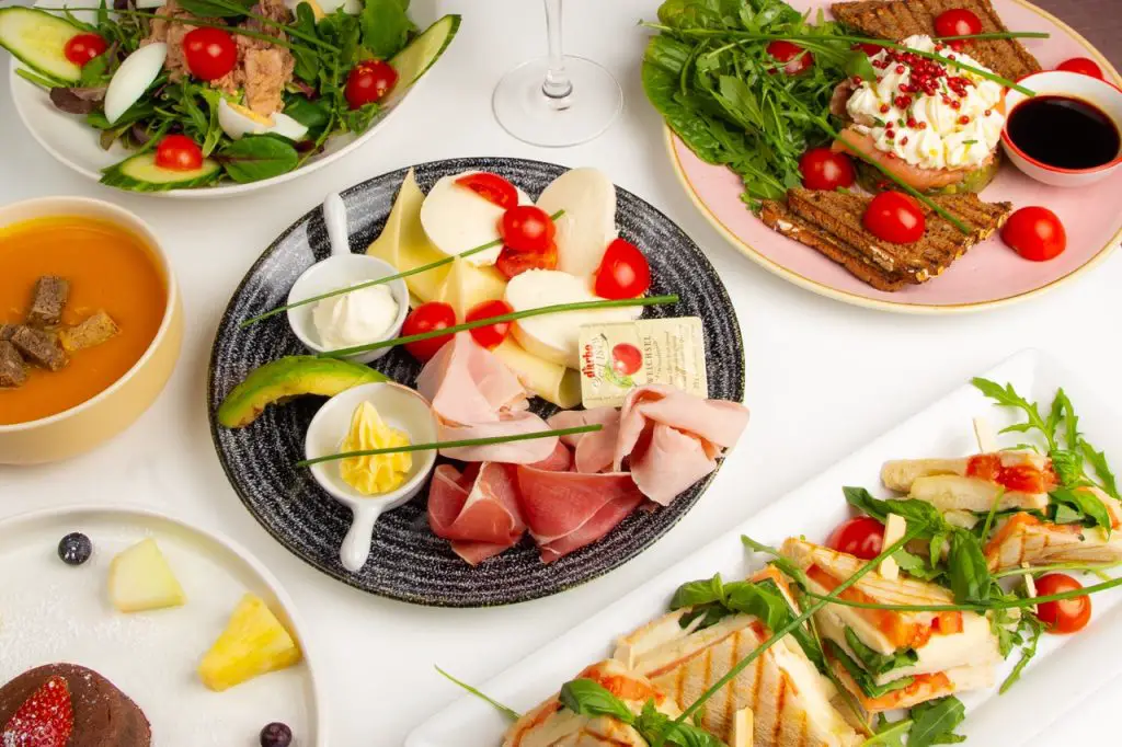 Eine Auswahl an vielfältigen Gerichten, darunter Salate, Suppen und belegte Brote, auf einem weißen Tisch.