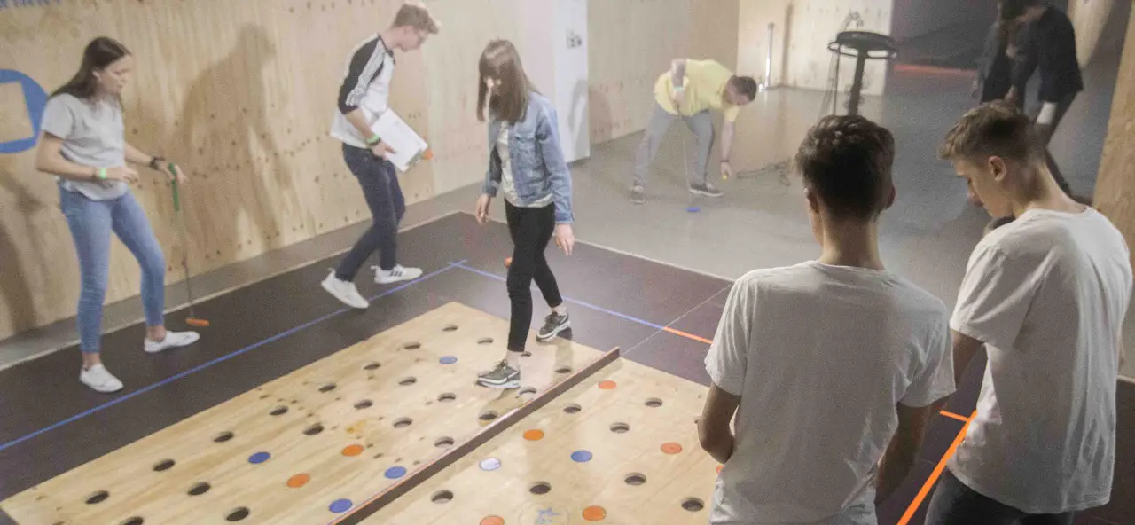 Junge Erwachsene spielen auf einer beleuchteten Indoor-Minigolfbahn mit farbigen Punkten.