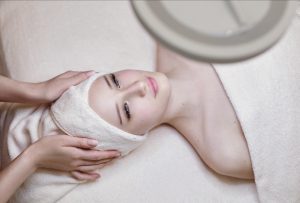 Junge Frau erhält eine entspannende Gesichtsbehandlung mit einem weißen Handtuch um den Kopf gewickelt.