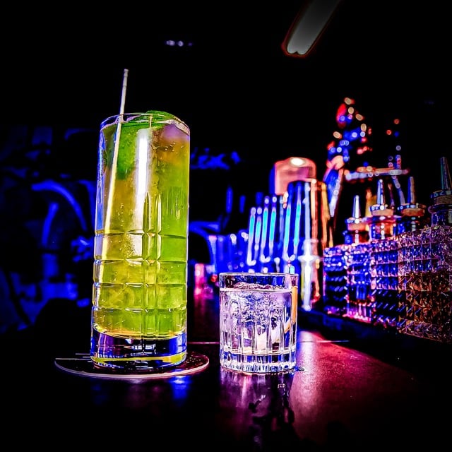 Die belebte Bar "The Pawn Dot Com" in Berlin Mitte bei Nacht, mit glänzenden Lichtern und Gästen, die Cocktails genießen.