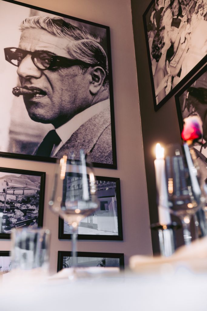 Schwarz-weiß Fotografie eines Mannes mit Zigarre an der Wand, unscharf davor stehen edle Weingläser und eine brennende Kerze im griechischen Restaurant Greek Food Olympia.