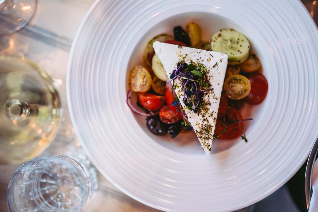Ein griechischer Salat mit frischen Tomaten, Gurken, Oliven und einem dicken Stück Feta, angerichtet auf einem weißen Teller im griechischen Restaurant Greek Food Olympia.