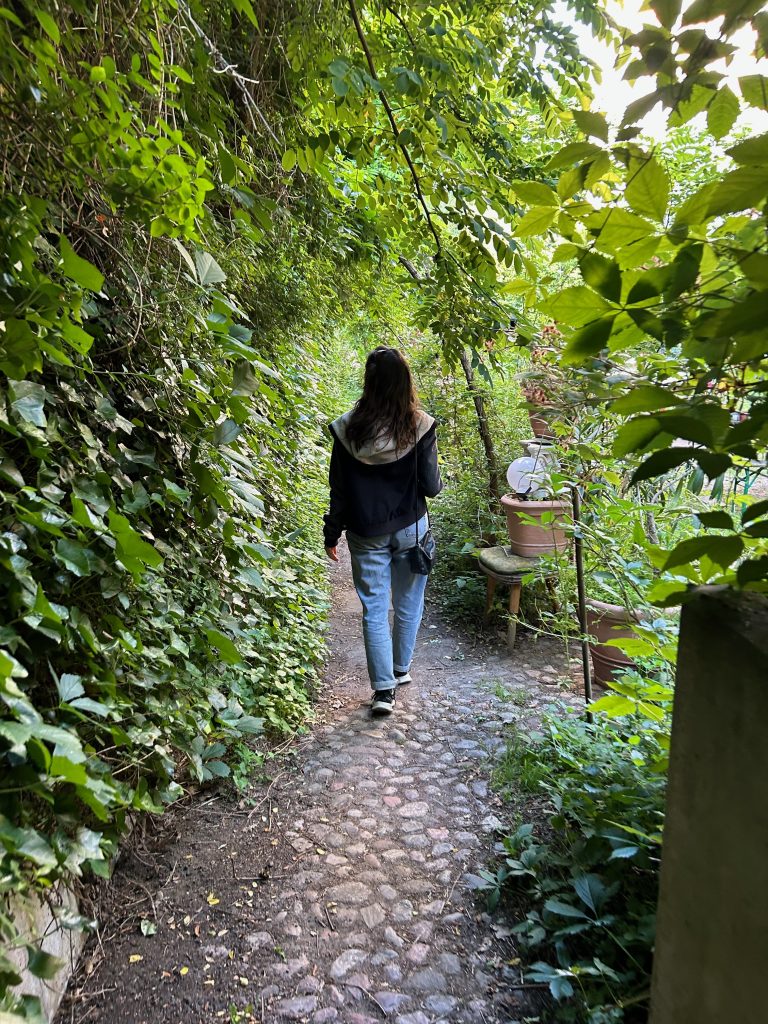 Frau spaziert allein auf einem schmalen, von dichtem Grün umgebenen Kopfsteinpflasterweg, der geheimnisvoll wirkt.