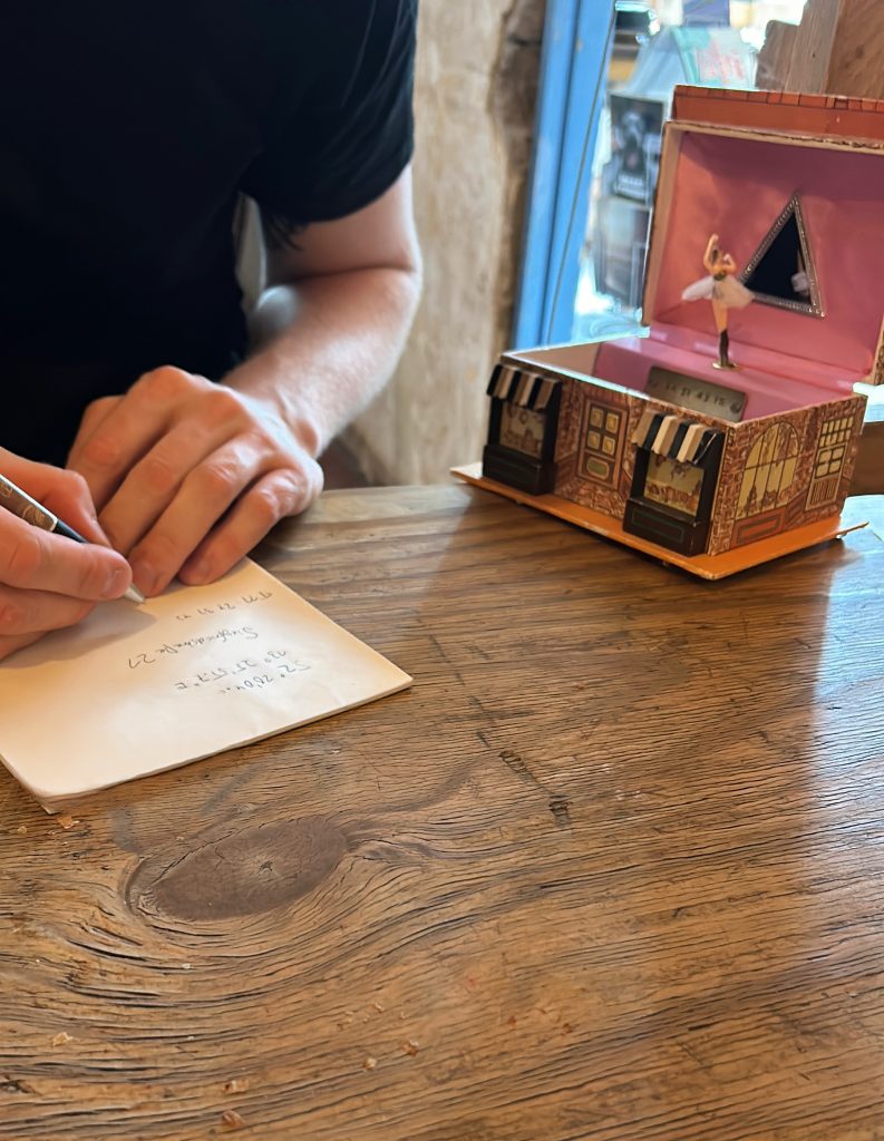 Person schreibt Notizen auf ein Blatt Papier neben einer Spieluhr mit Ballerina auf einem Holztisch.