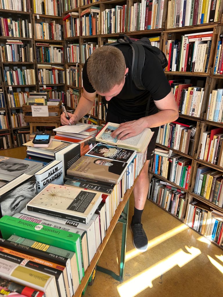 Person vertieft sich in ein Buch in einem hellen Buchladen, mit Smartphone daneben.